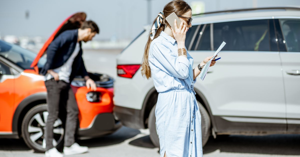 A woman standing beside a damaged car using a cellphone, while a man checks the two vehicles on the road.
