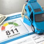 A credit score report with various information laying on a grey desk covered in hundred dollar bills and a small toy car.