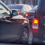 Multiple black cars and SUVs are closely following one another. They all have illuminated taillights.