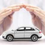 A close-up of a person cupping their hands together to cover the top of a small, white toy car sitting on a table.