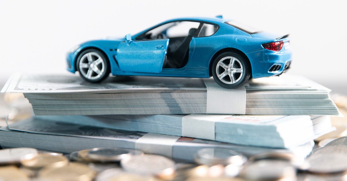 A small blue toy car sits on top of large stacks of cash bundled together. Around the cash is a pile of coins.