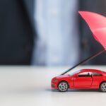 A person wearing a suit sits at a table. In front of them is a red toy car with a tiny umbrella propped over it.