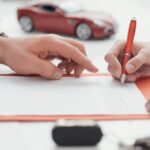 Two people sit across from one another at a desk. One person holds a pen, while the other points to a piece of paper.