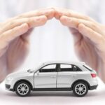 A set of hands arching together to cover a small, white model car. The background is also a bright white.