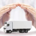 A person in a white long-sleeved shirt sitting at a table while holding both hands over a toy truck.
