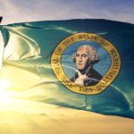 The Washington state flag flaps in the wind, featuring George Washington's face. The sun sets in the background.
