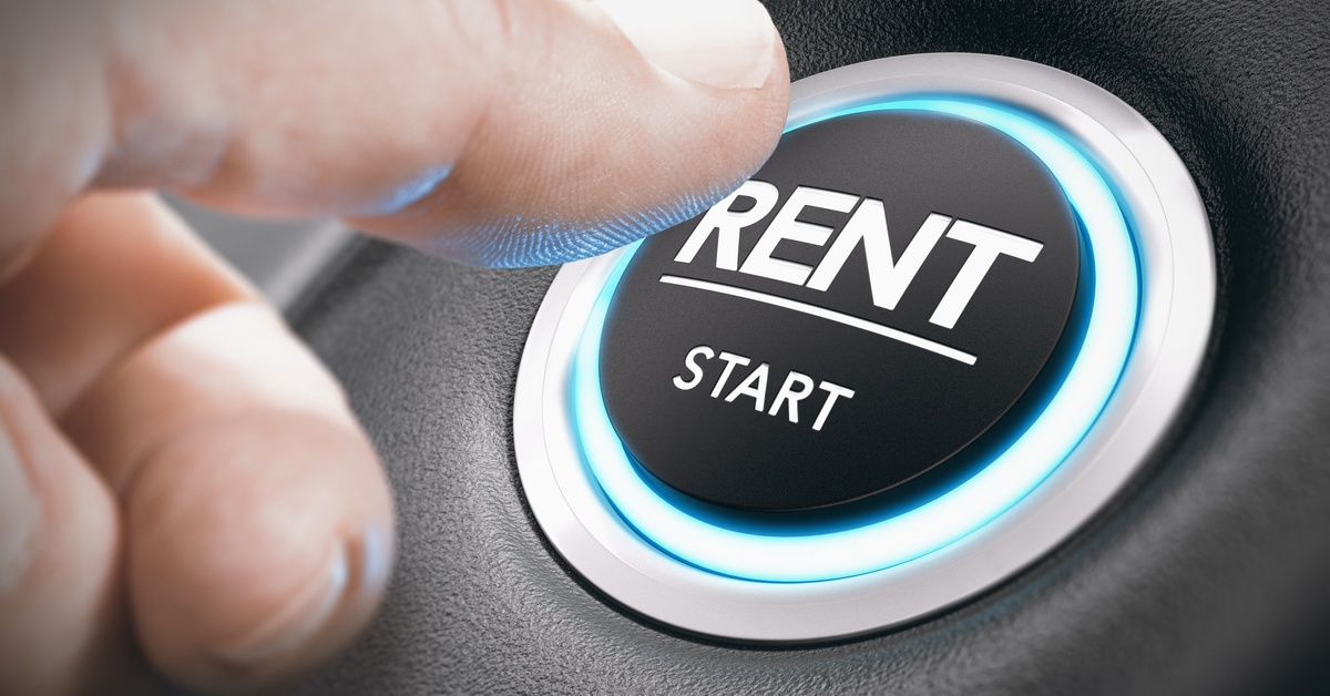 Close-up of a thumb reaching over to press a shining button labeled "RENT -- START" on a car's dashboard.