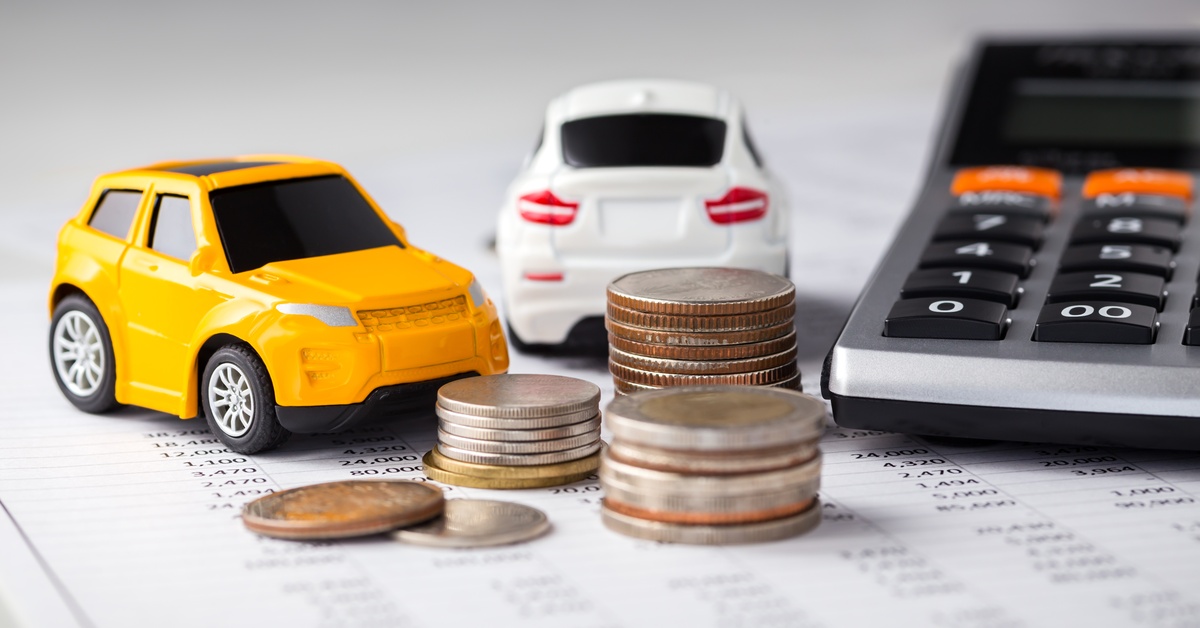 A pair of toy cars sits on sheets of paper with numbers next to several stacks of coins and a calculator.