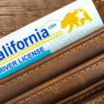 A wallet lies on a wooden table. A card reading "California Driver License" sticks out of one of the pockets.