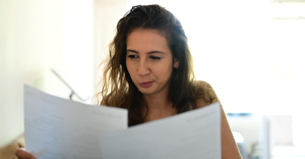 A woman smiles as she carefully looks over documents that she holds in each hand. She has black hair.