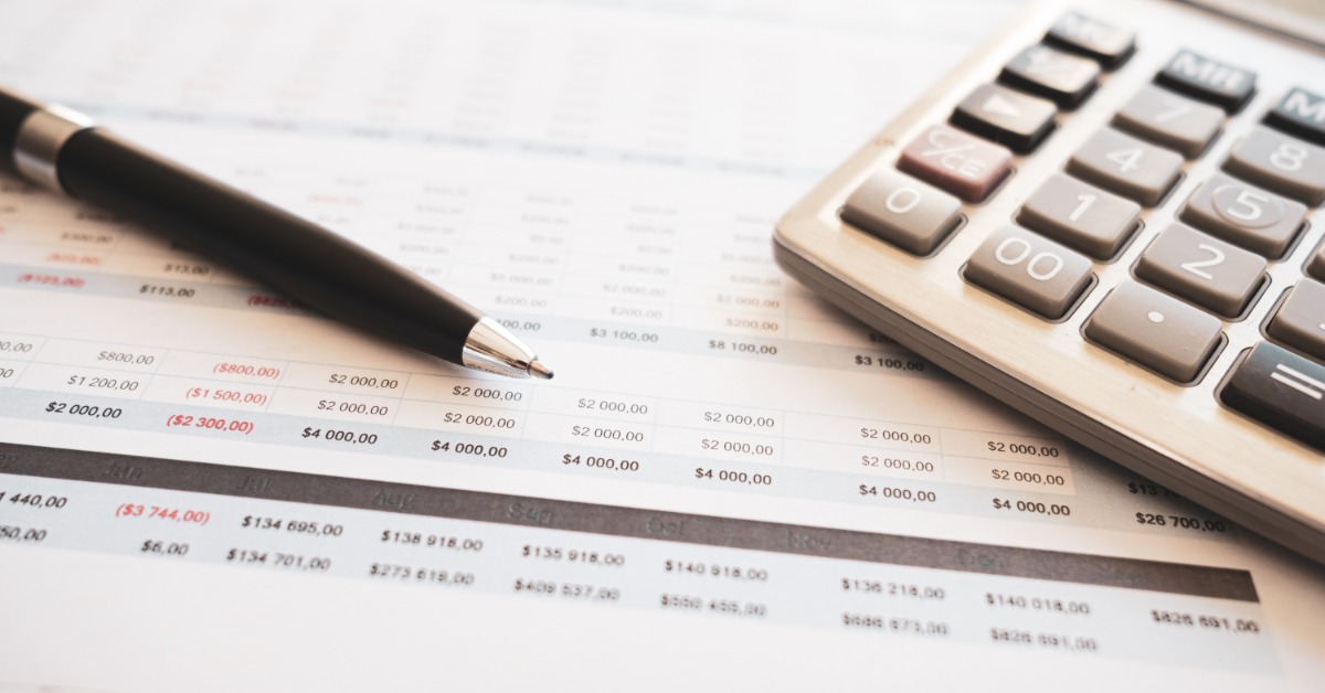 Close-up of a pen and a calculator lying on top of a budgeting spreadsheet on a flat surface. The pen is black and silver.