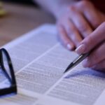 A pair of hands holds a smartphone in front of a car steering wheel. The screen shows the words "Car Insurance."