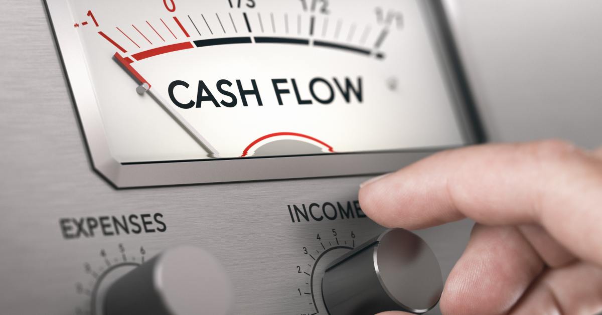 Close-up of a person's hands about to turn a knob labeled "Income" on a meter that reads the words "Cash Flow."