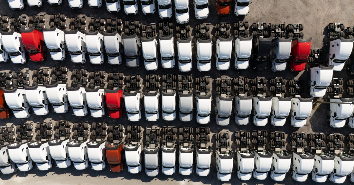 Overhead view of a crowded parking lot filled with red and white parked trucks. Daylight shines down on them.