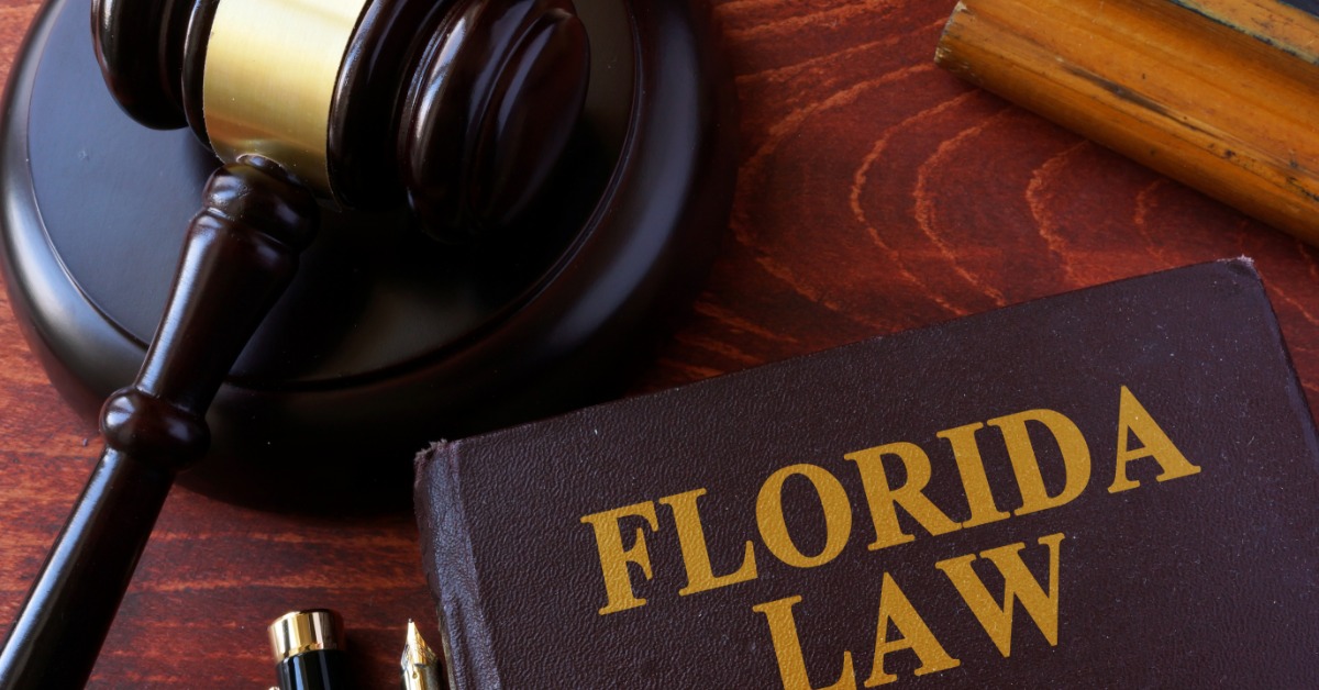 A gavel, pen, and book titled Florida Law sit arranged on a wooden tabletop. A wooden block sits nearby on the table.