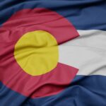 A Colorado state flag features a large red C surrounding a yellow sun. It also has blue and white stripes.